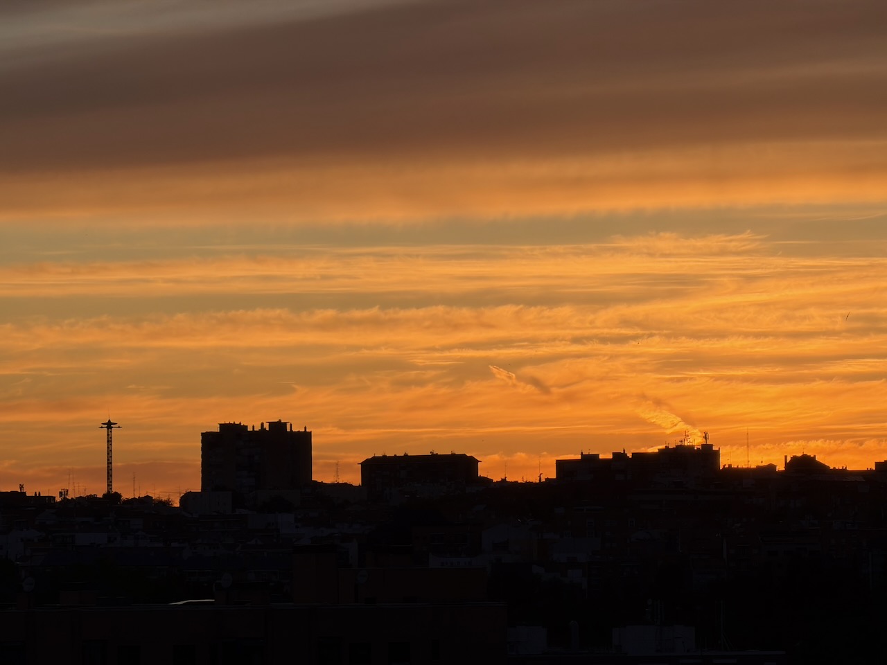 Silhouetted cityscape against a vibrant orange and yellow sunset sky.