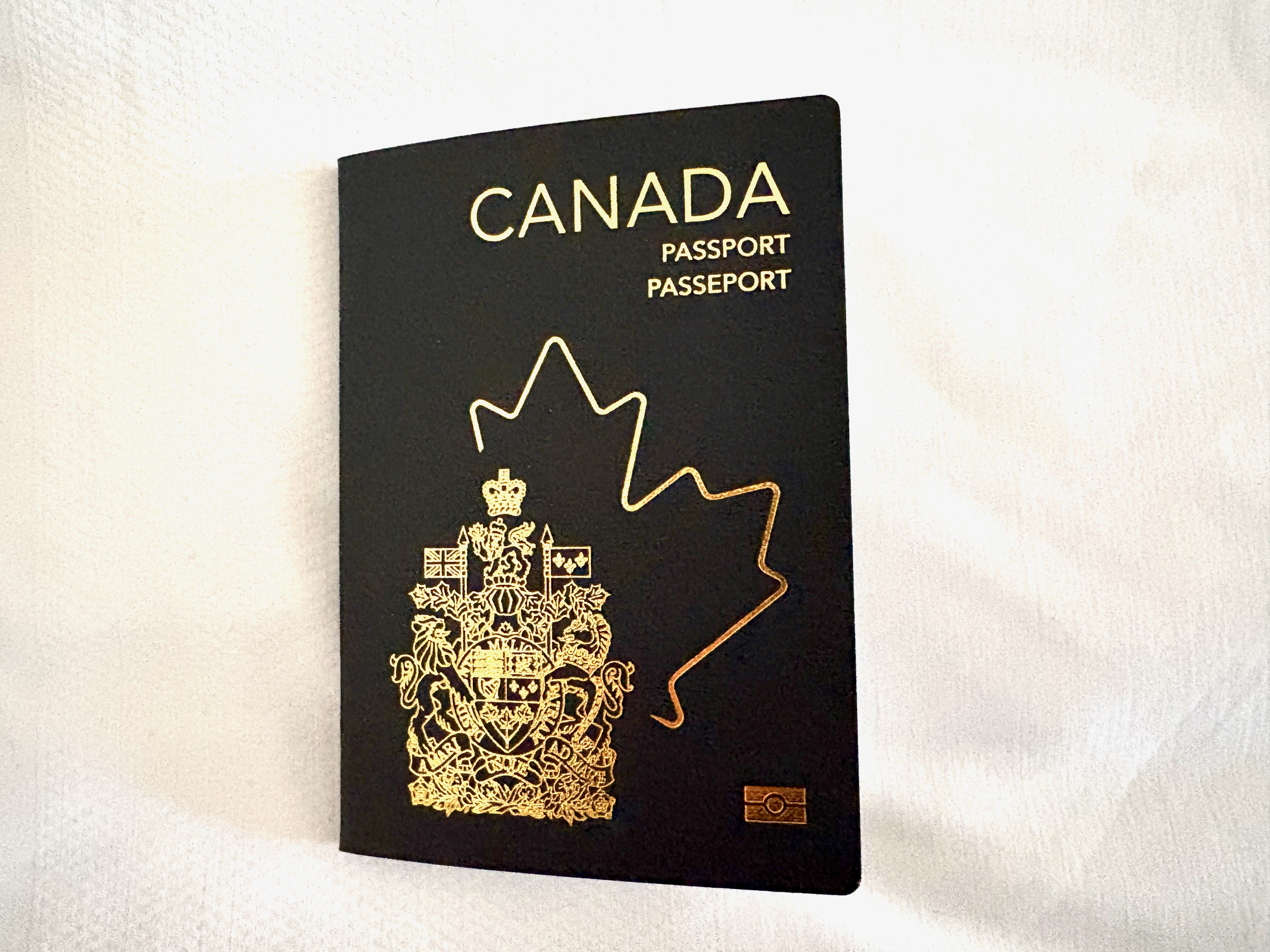 Canadian passport with gold maple leaf and coat of arms on black cover.