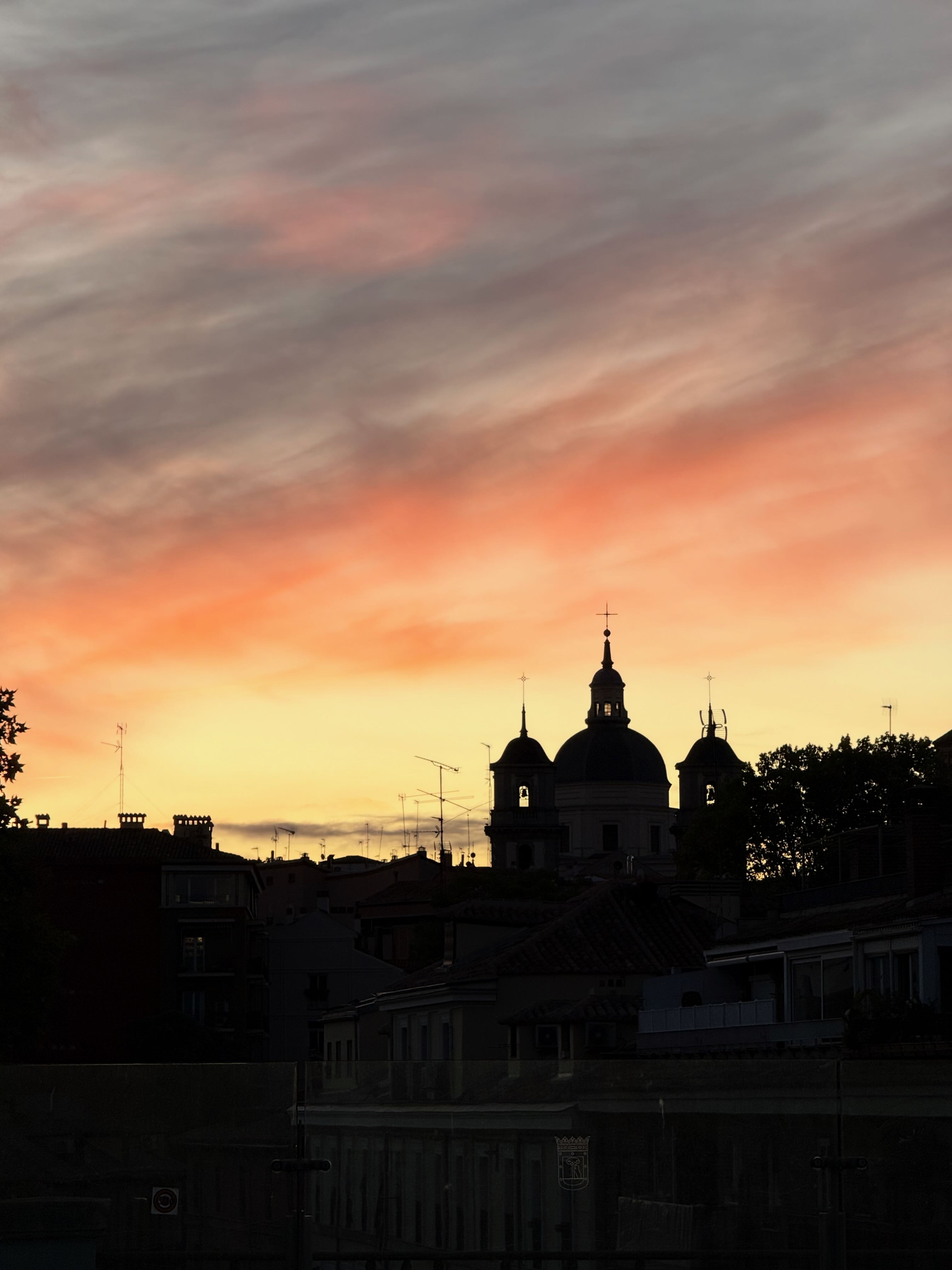 Silhouetted buildings and domes against a vibrant sunset sky with orange and pink hues.
